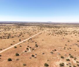 Wide drone shot looking north across open desert with road through the parcel and distant mesa, Navajo County AZ — parcel 111-22-195